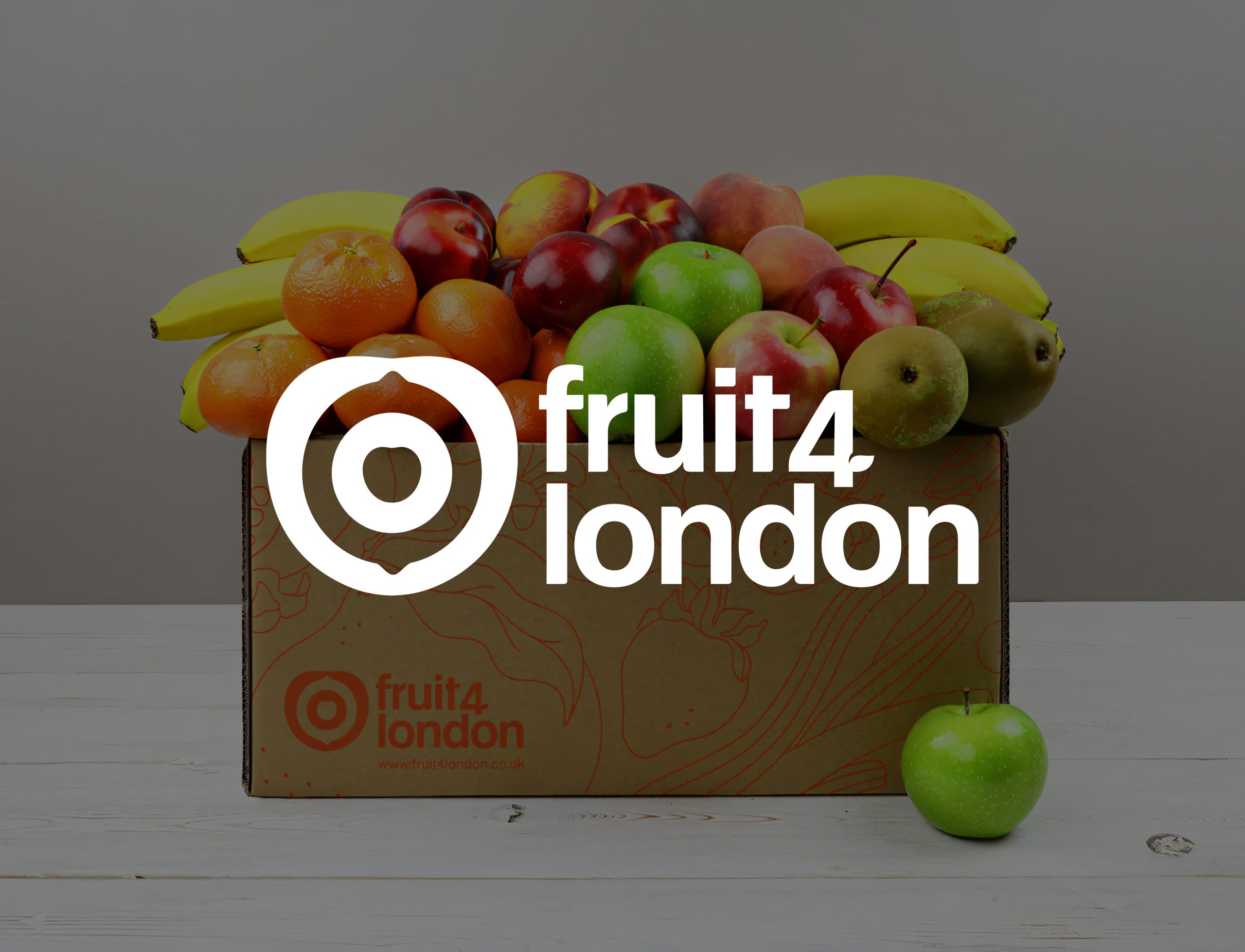 A box of assorted fruit against a grey background with the Fruit 4 London logo displayed on top