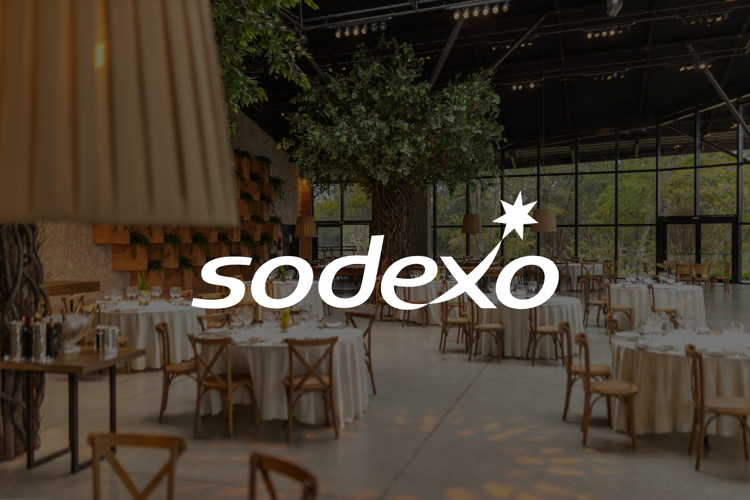 A garden scenery with tables and chairs on a patio with the Sodexo logo displayed on top
