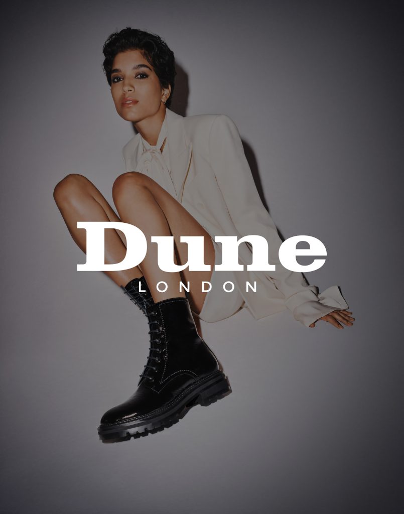 Dune-London-Ecommerce A woman wearing black boots sitting against a white background with the Dune London logo displayed on top