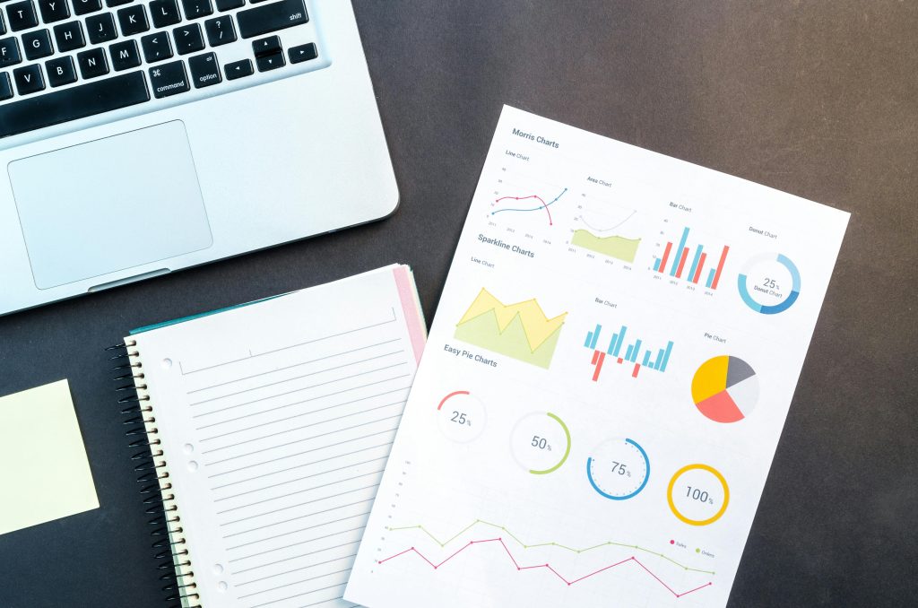 pexels-goumbik-669619 A sheet of paper containing colourful pie charts and analytical data on a black table next to a laptop